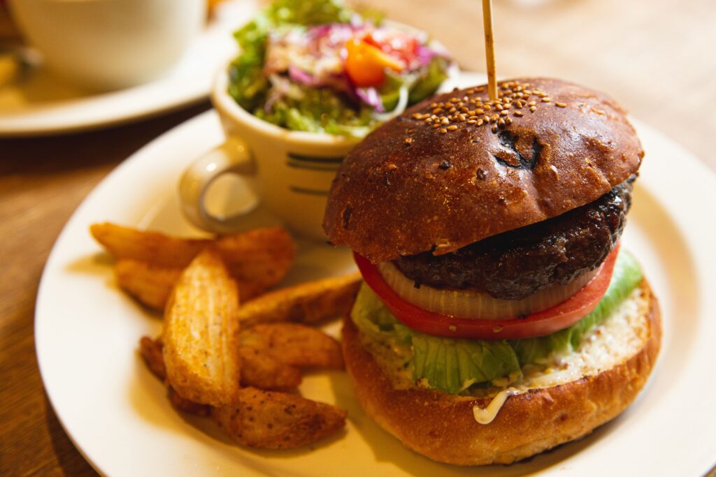 High angle of appetizing hamburger with cutlet and vegetables served on plate with salad and fried potatoes